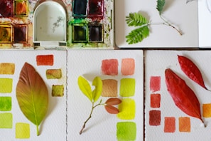 A flat lay of printed coloring pages with autumn leaves and gentle patterns on a wooden table.