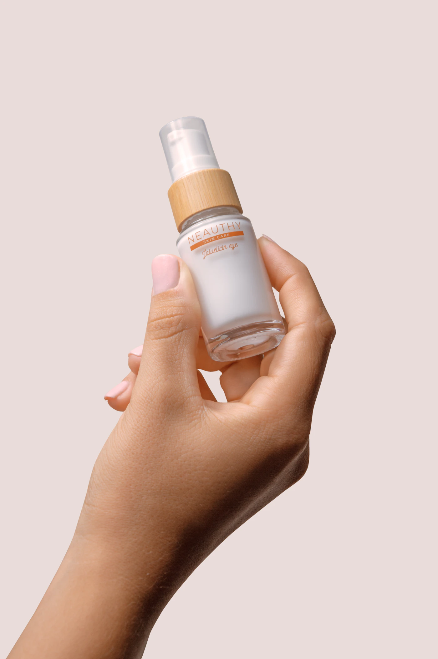 Hand holding a small white bottle of face serum against a pink backdrop