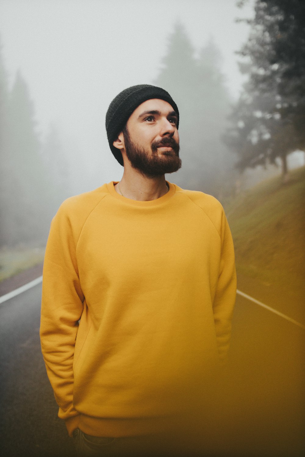 黄色いタートルネックのセーターを着た男が緑の草原のそばに立つ