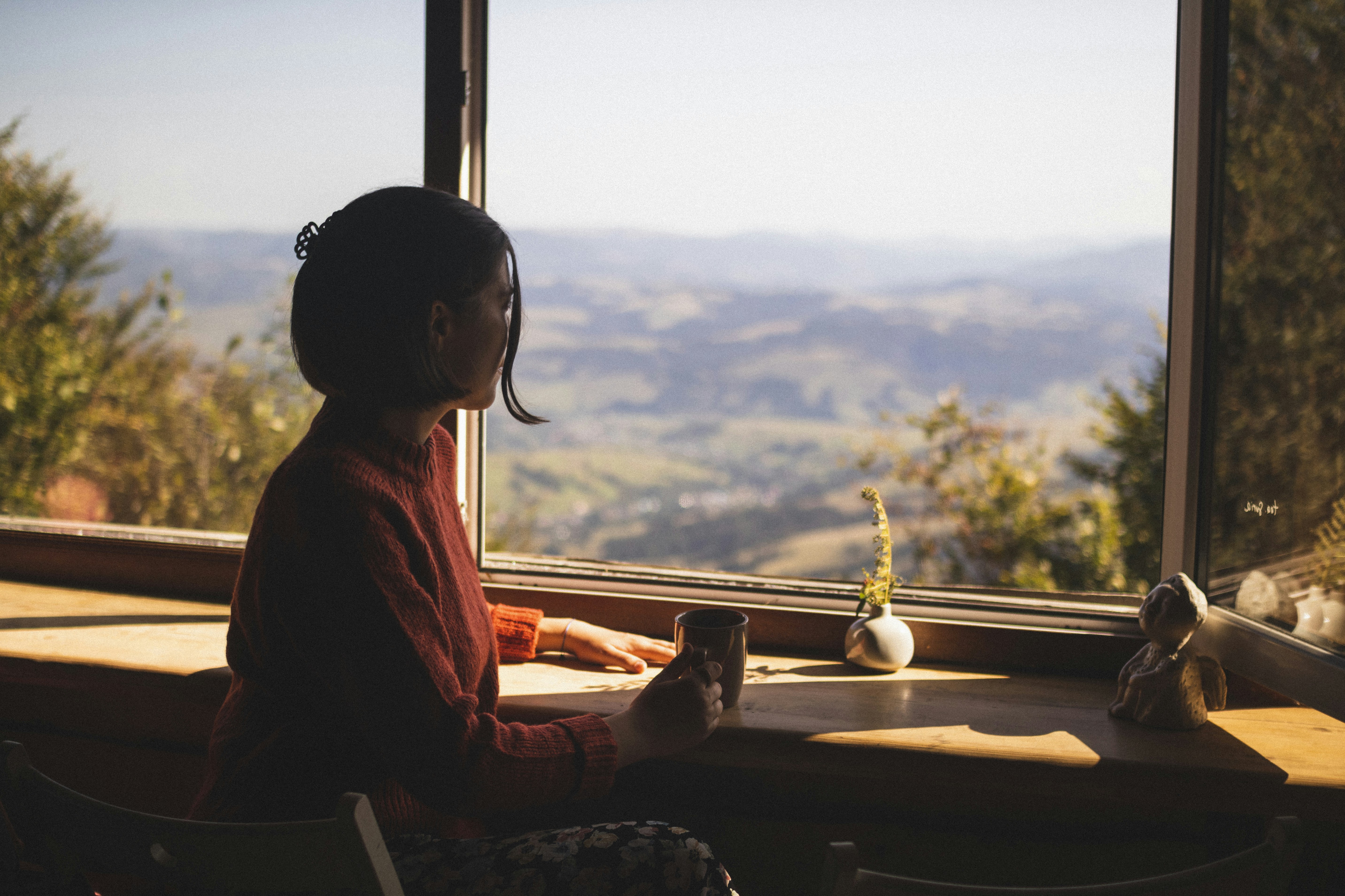 woman in red long sleeve shirt sitting on chair looking at the window during daytime
