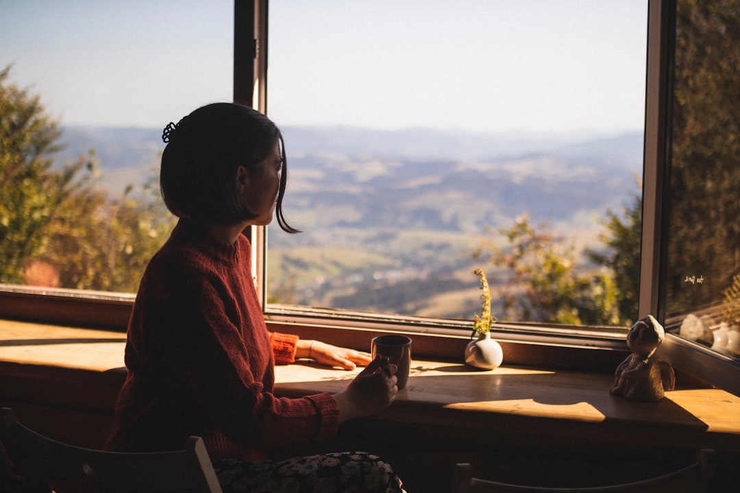 woman in red long sleeve shirt sitting on chair looking at the window during daytime