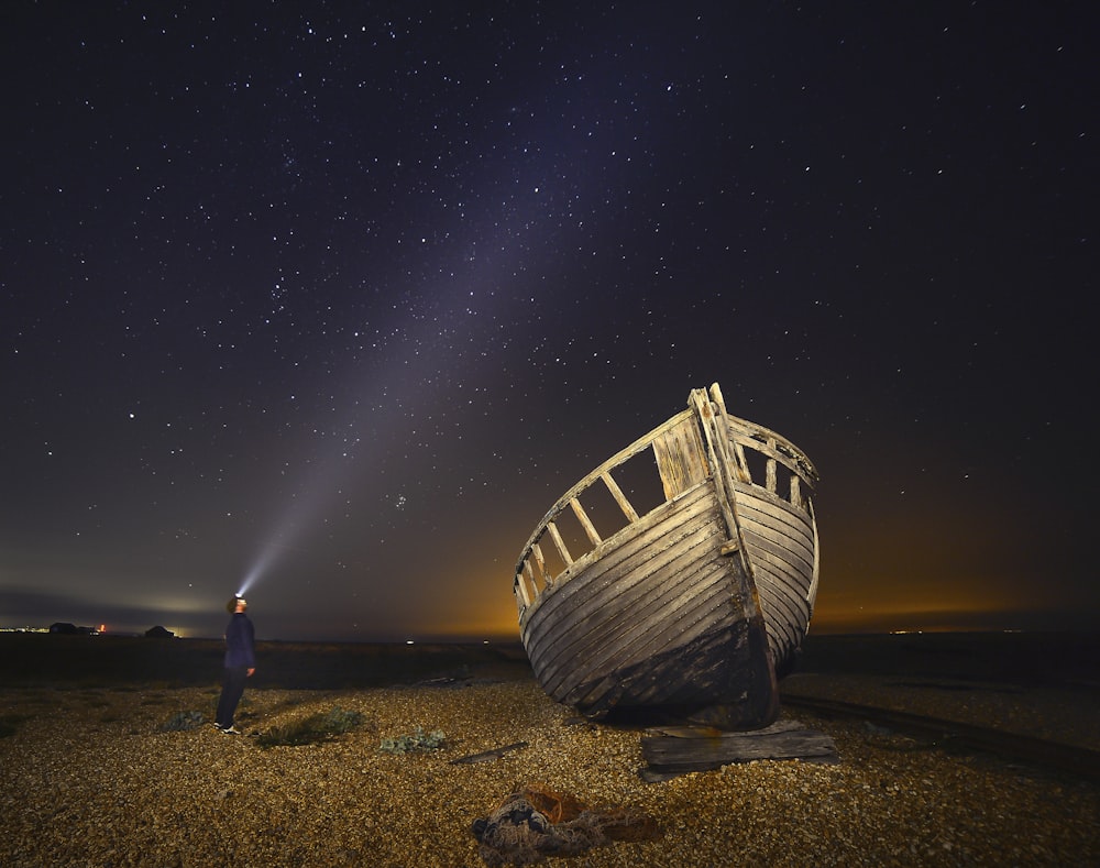 hombre de pie junto a un barco de madera marrón bajo la noche estrellada