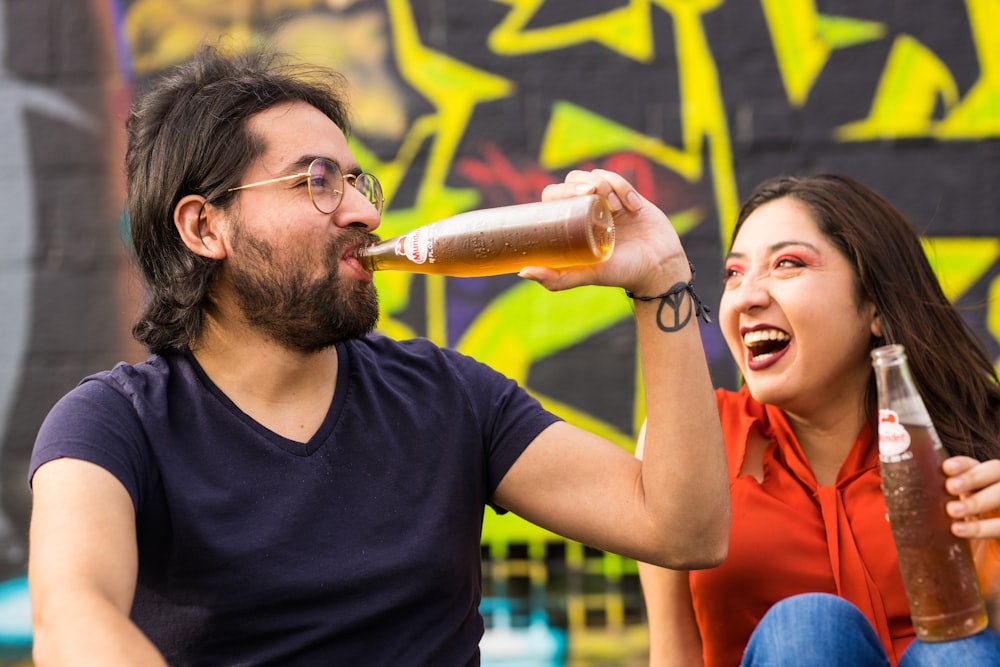 man in black crew neck t-shirt holding woman in red sleeveless dress drinking beer