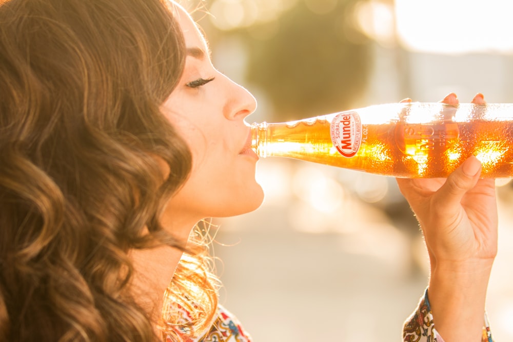 mulher que bebe líquido laranja da garrafa