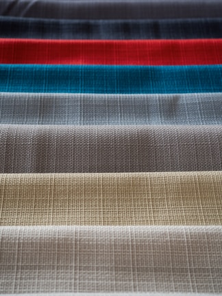 Rows of fabric swatches in various textures and colors spread out on a polished table.