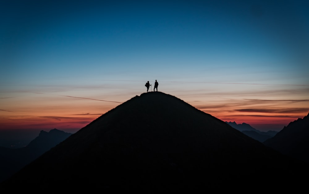 silueta de la persona de pie en la cima de la montaña durante el día