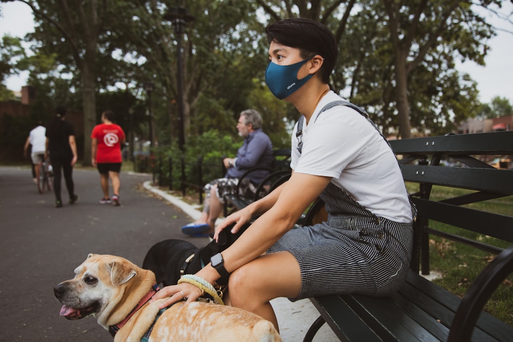 man in white t-shirt sitting on bench beside brown dog