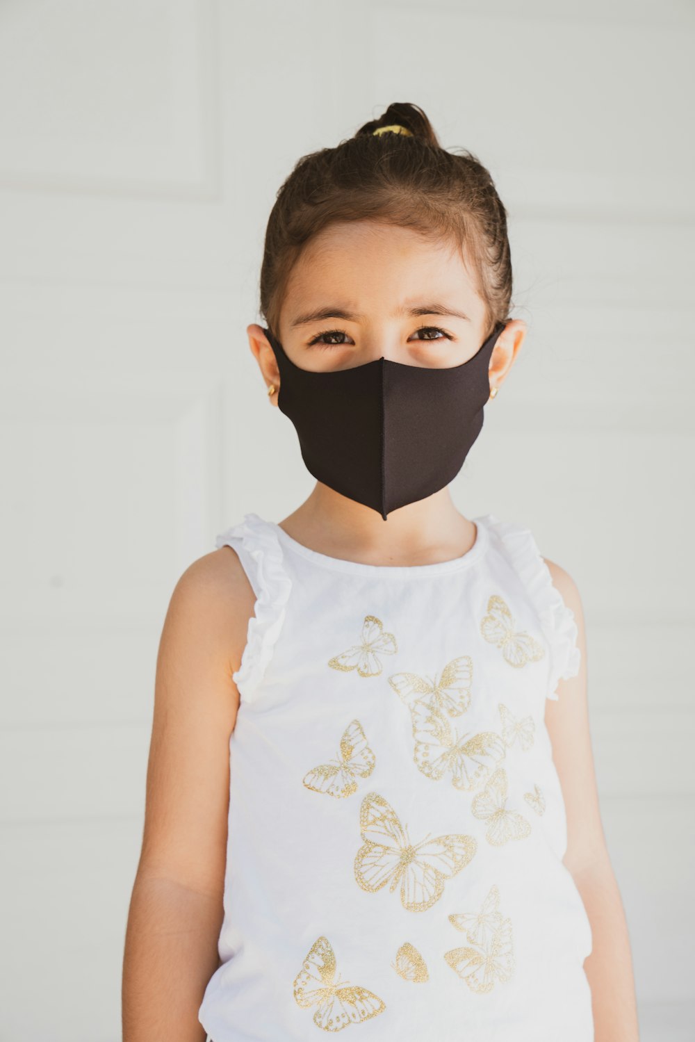 Mädchen in weißem geblümtem Tanktop mit schwarzer Gesichtsmaske