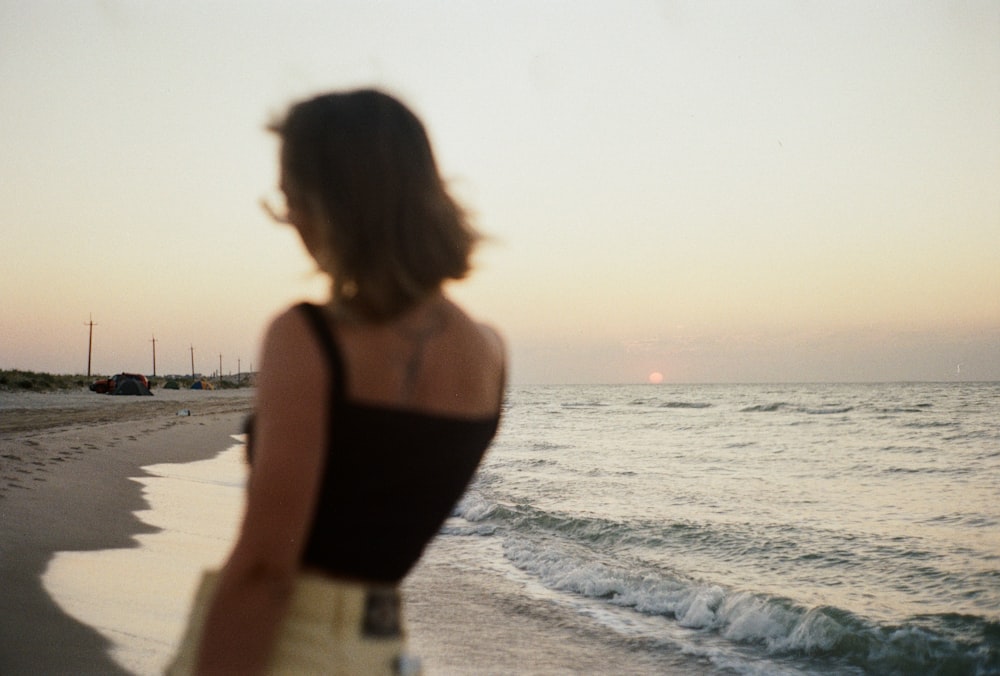 Mujer con camiseta sin mangas negra de pie en la playa durante el día