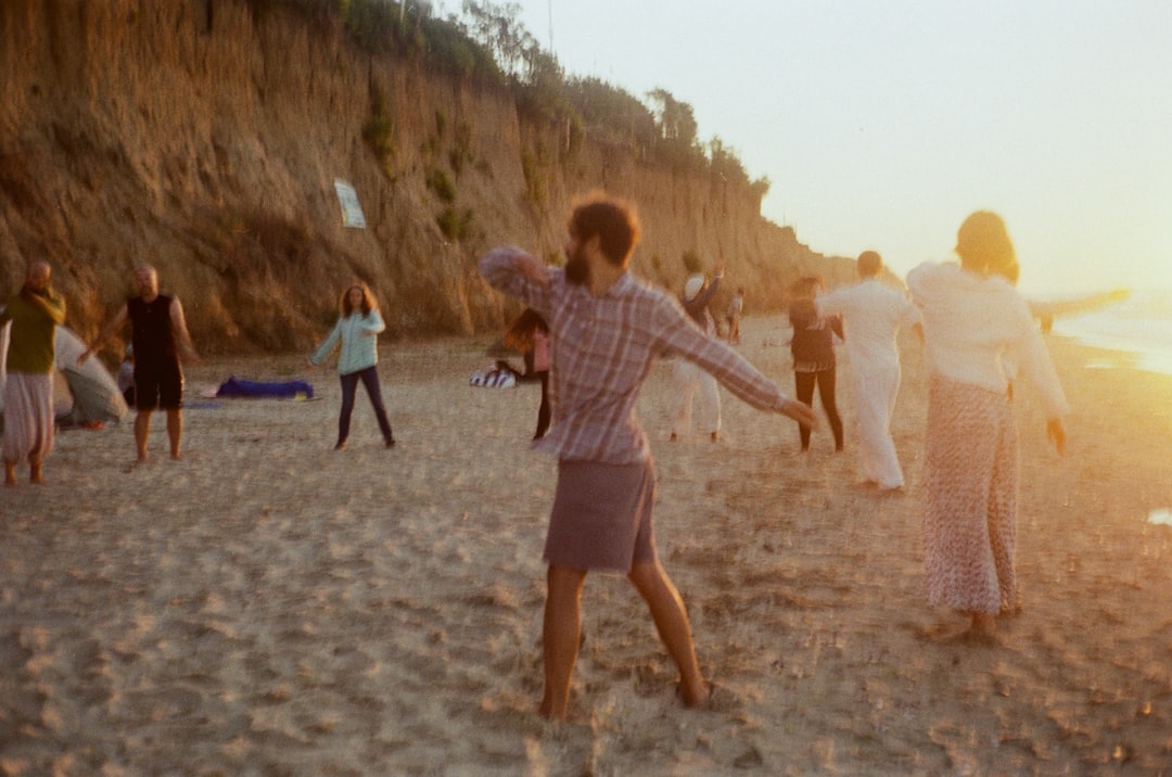 man in white and gray stripe shirt and black shorts walking on brown sand during daytime