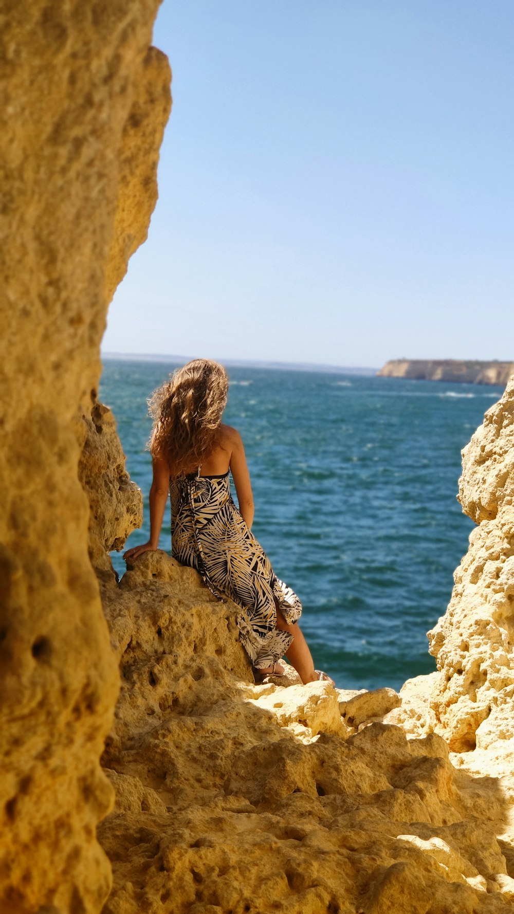 woman in black and white floral spaghetti strap dress standing on brown rock formation near body