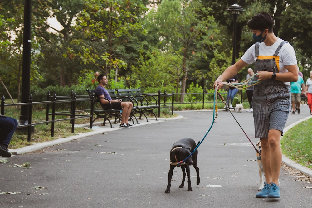 man in white t-shirt and blue shorts holding black short coat dog