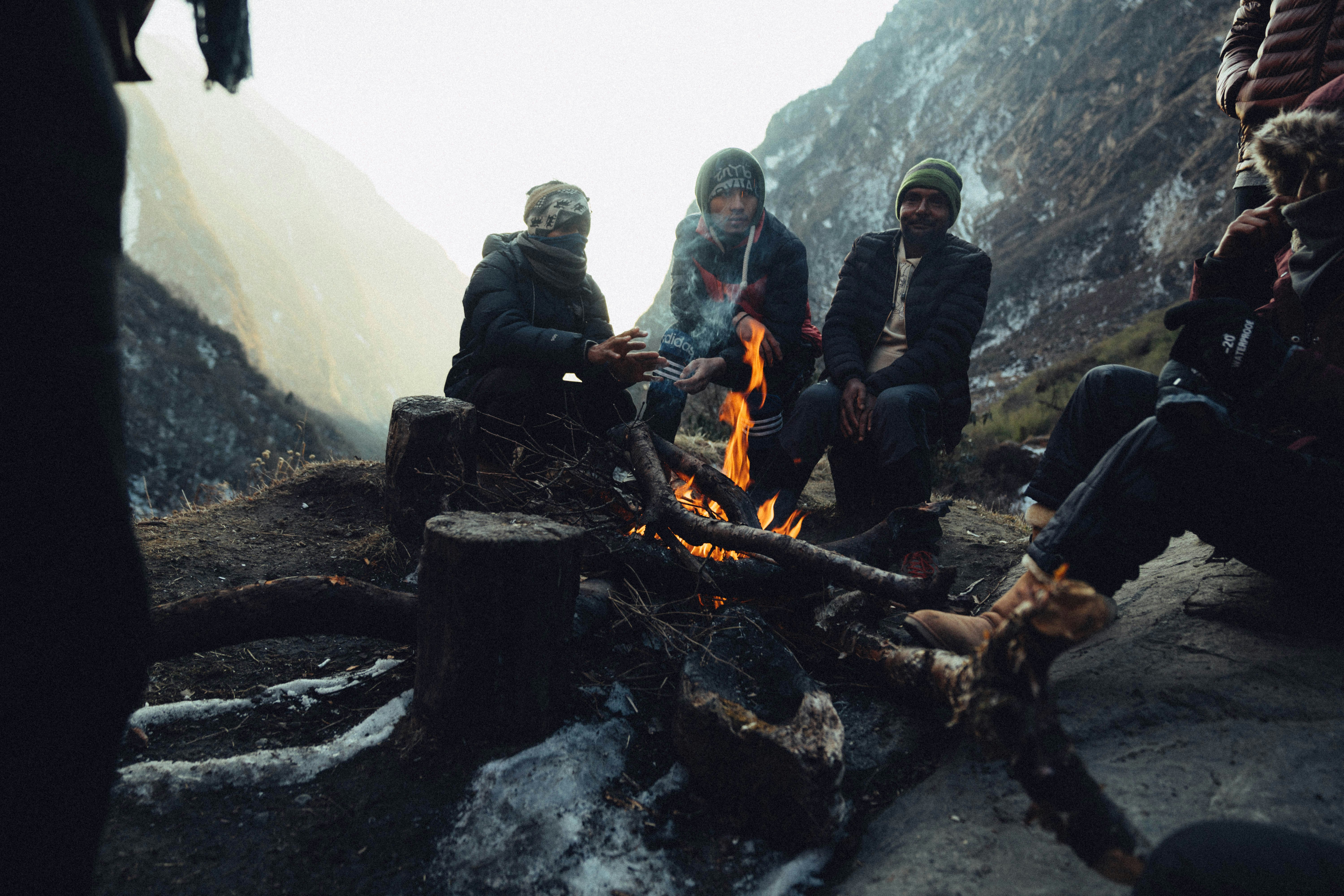 3 men in black jacket sitting on black metal fire pit during daytime