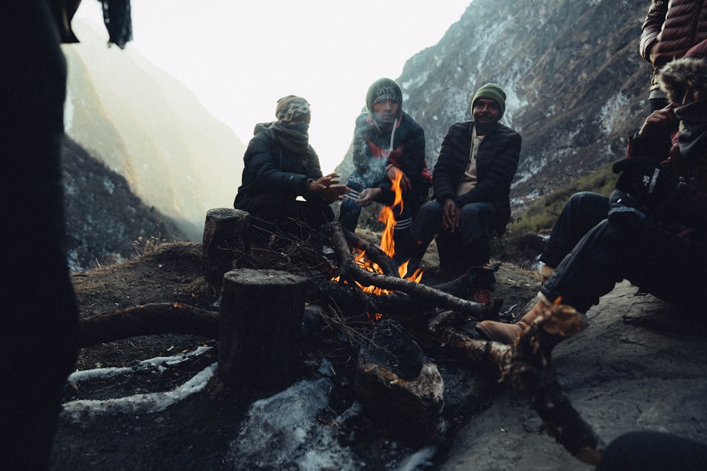 3 hombres con chaqueta negra sentados en un pozo de fuego de metal negro durante el día