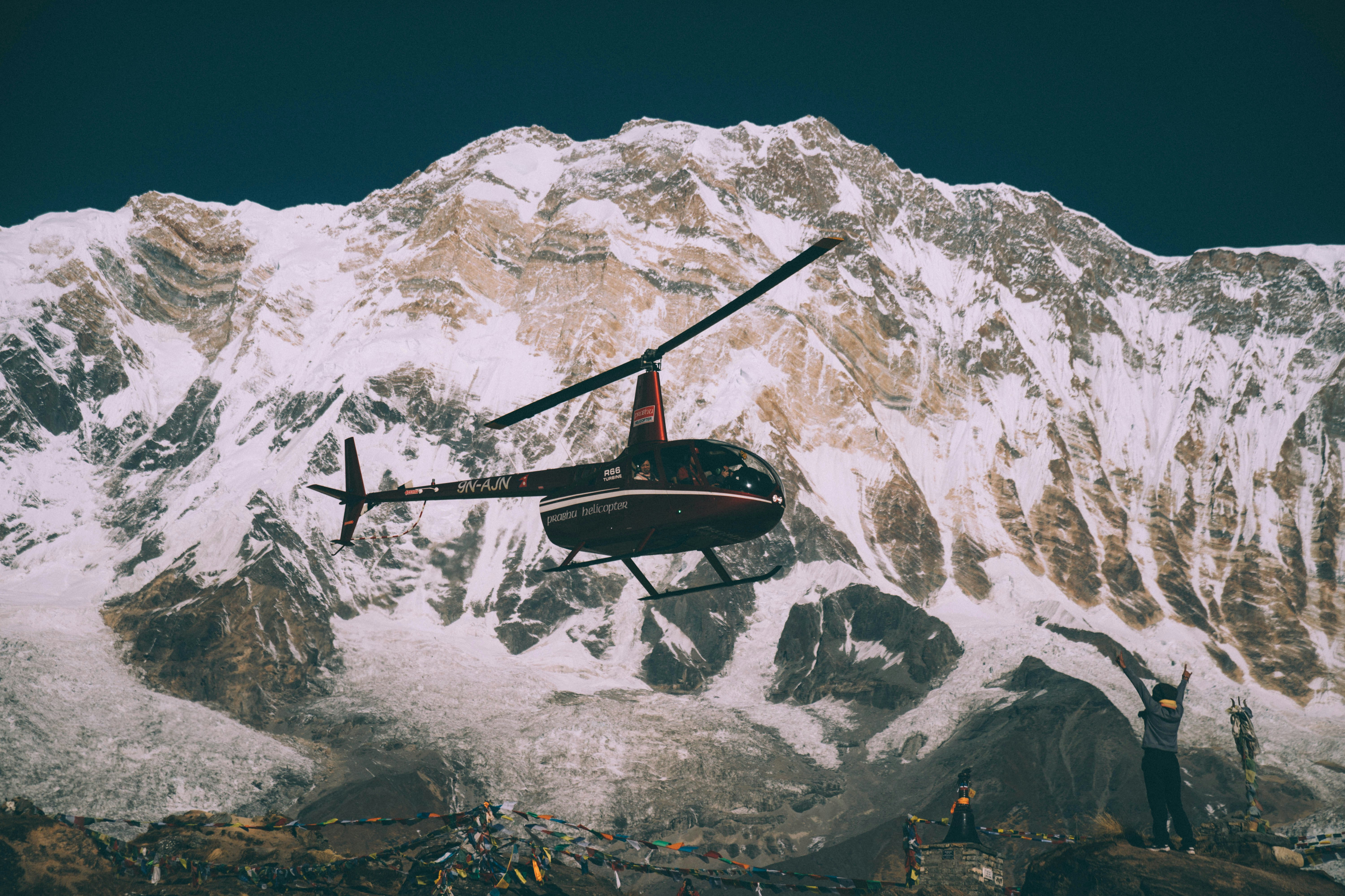 black and red helicopter flying over snow covered mountain during daytime