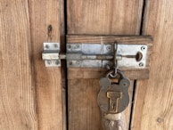 A close-up view of a wooden door featuring a sturdy metallic latch secured with an old-fashioned padlock, showcasing a rustic and weathered appearance.
