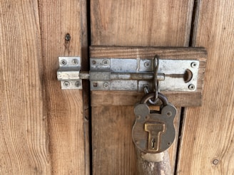 A close-up view of a wooden door featuring a sturdy metallic latch secured with an old-fashioned padlock, showcasing a rustic and weathered appearance.