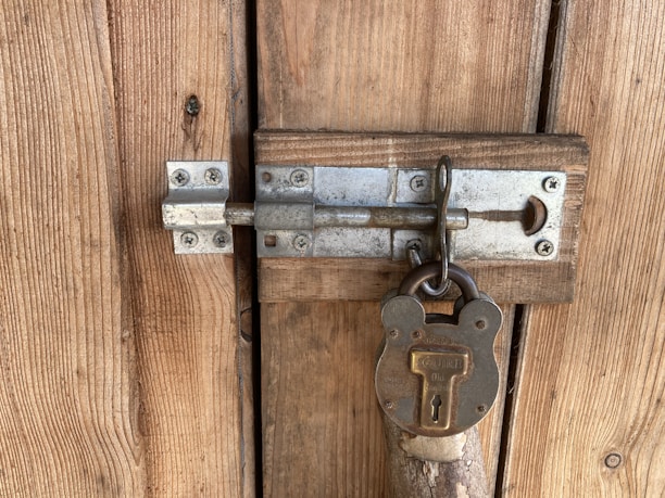 A close-up view of a wooden door featuring a sturdy metallic latch secured with an old-fashioned padlock, showcasing a rustic and weathered appearance.