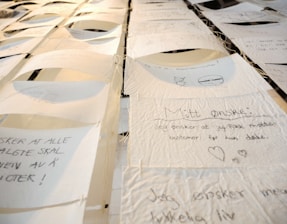 A collection of handwritten notes on thin, textured paper, suspended and displayed in rows. Each note contains text and small drawings, with varying handwriting styles. The setting appears artistic, with a focus on personal expressions or wishes.