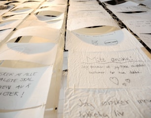 A collection of handwritten notes on thin, textured paper, suspended and displayed in rows. Each note contains text and small drawings, with varying handwriting styles. The setting appears artistic, with a focus on personal expressions or wishes.