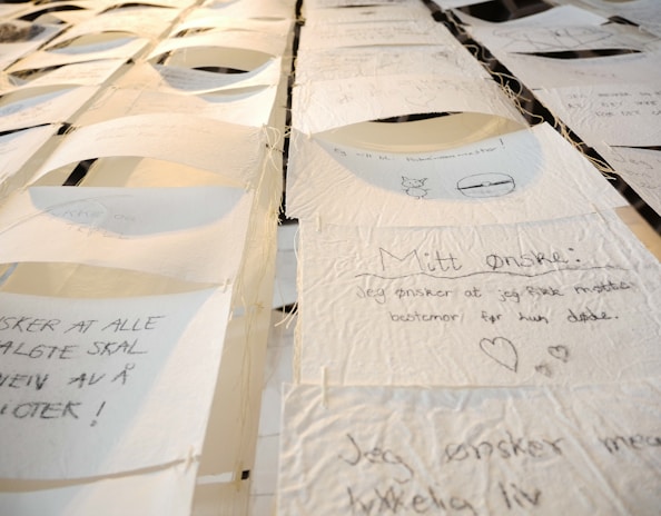 A collection of handwritten notes on thin, textured paper, suspended and displayed in rows. Each note contains text and small drawings, with varying handwriting styles. The setting appears artistic, with a focus on personal expressions or wishes.