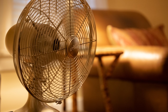 A sleek mini portable fan on a wooden table, surrounded by a peaceful outdoor setting.