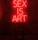 A dark room features a bright red neon sign displaying the words 'SEX IS ART'. In front of the sign, a black chair is silhouetted against the red glow.