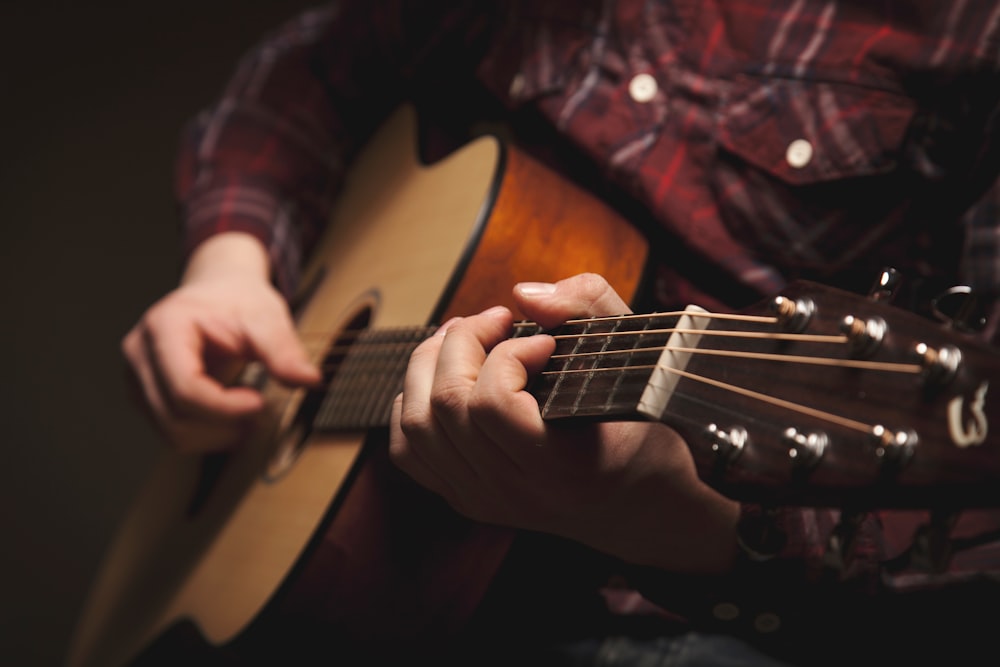 person playing brown acoustic guitar