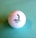 A golf ball with a textured surface placed on a light blue background. The ball features a logo of a person engaged in a golfing stance, accompanied by the text 'PINEHURST 1895'.