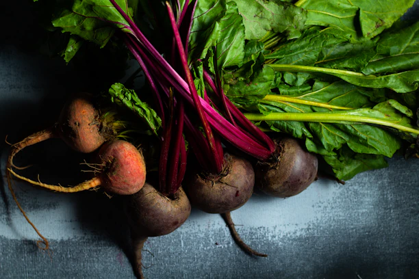 Close-up of vibrant beetroot powder in a rustic ceramic bowl surrounded by fresh beets and green leaves.
