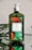 A green bottle of hand soap with a white pump sits on a reflective surface. The label on the bottle features images of oranges and green leaves, indicating the scent is 'Orange Blossom'. Some green foliage is visible in the background, complementing the natural theme of the product.