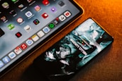 A smartphone and a tablet are placed on a surface with a warm lighting ambiance. The smartphone screen displays an artistic, abstract wallpaper, while the tablet shows a variety of colorful application icons, including Google, Netflix, and others.