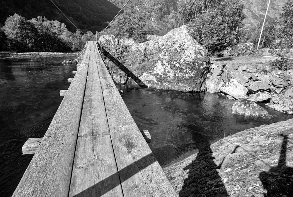 grayscale photo of wooden bridge over river
