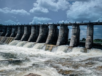 A large dam structure with water flowing through spillways under a clear sky.