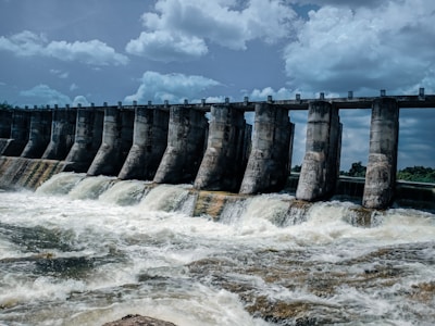 A large dam structure with water flowing through spillways under a clear sky.