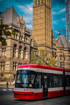 red and white tram in front of brown concrete building during daytime