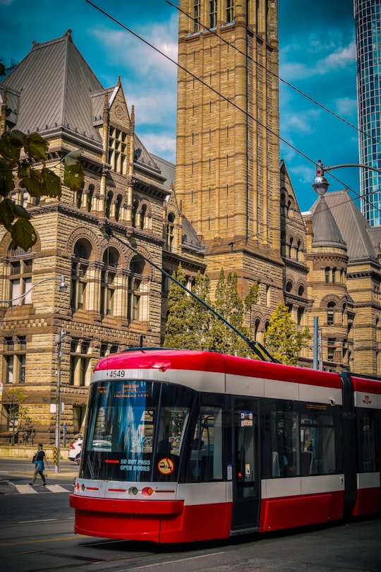 red and white tram in front of brown concrete building during daytime in Old City Hall Canada