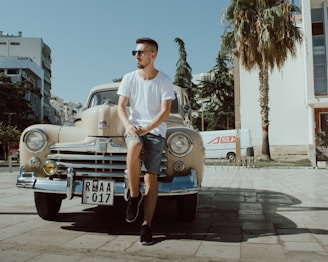 man in white crew neck t-shirt and blue denim shorts sitting on blue car