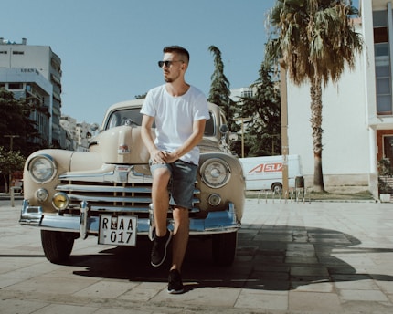 man in white crew neck t-shirt and blue denim shorts sitting on blue car