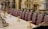 An opulently decorated dining room with a long table lined with plush, high-backed chairs upholstered in rich red leather. The table is adorned with ornate gold candelabras, and the room features intricate gold detailing and dark wood paneling. Classical architectural elements are present, illustrating a sense of luxury and grandeur.