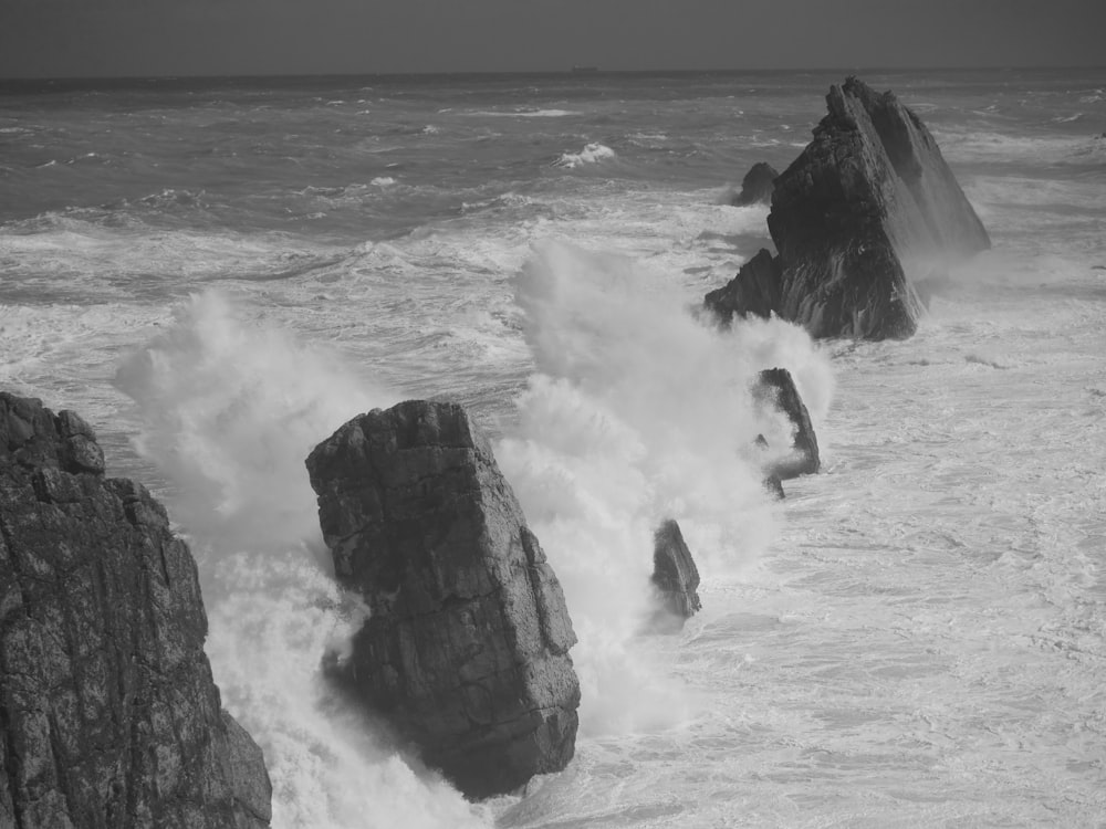 grayscale photo of sea waves crashing on rock formation