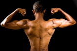 A muscular person flexing their arms to showcase well-defined back and arm muscles against a dark background.
