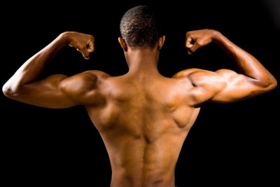 A muscular person flexing their arms to showcase well-defined back and arm muscles against a dark background.