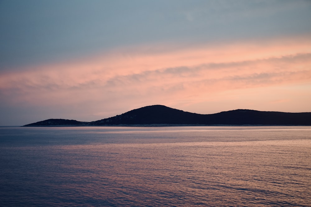 silhouette of mountain near body of water during sunset