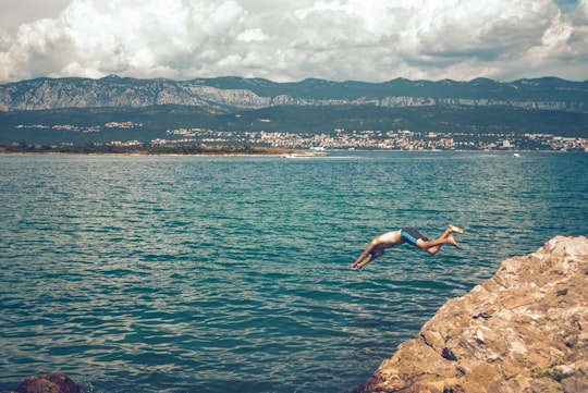 person jumping on rocky shore during daytime in Krk Croatia