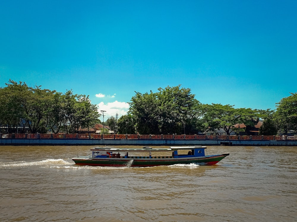 weißes und blaues Boot tagsüber auf dem Wasser in der Nähe grüner Bäume