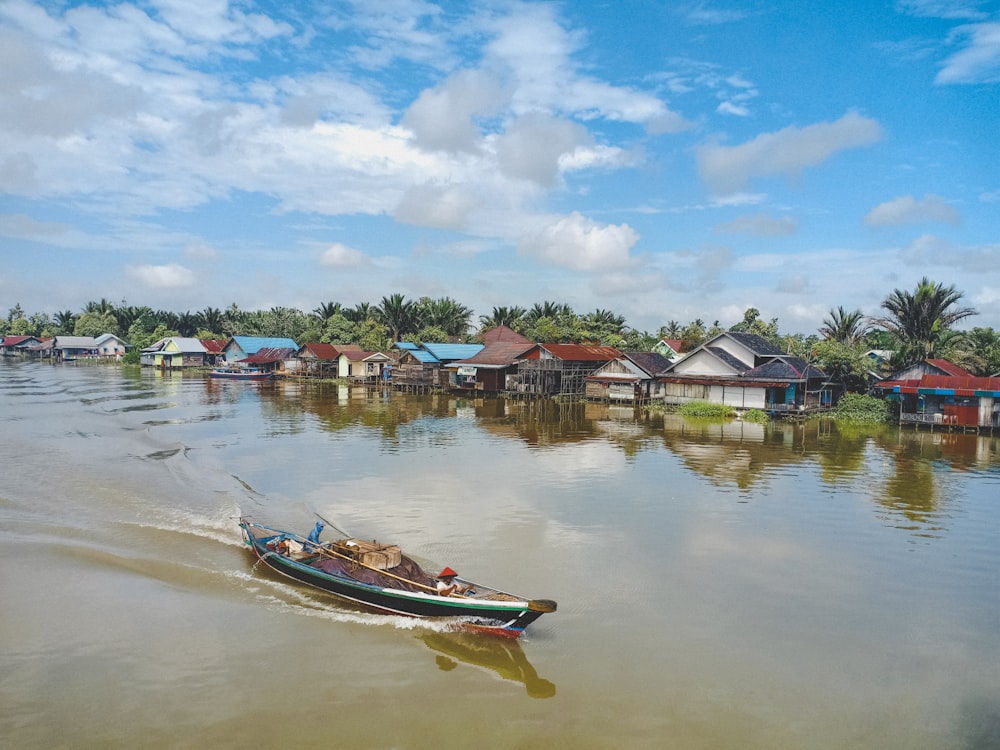 weißes und rotes Boot tagsüber auf dem Wasser in der Nähe von Häusern unter blauem Himmel