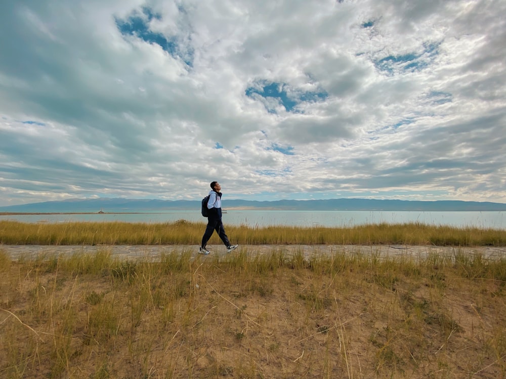 mulher na jaqueta preta em pé no campo de grama marrom sob nuvens brancas e céu azul durante
