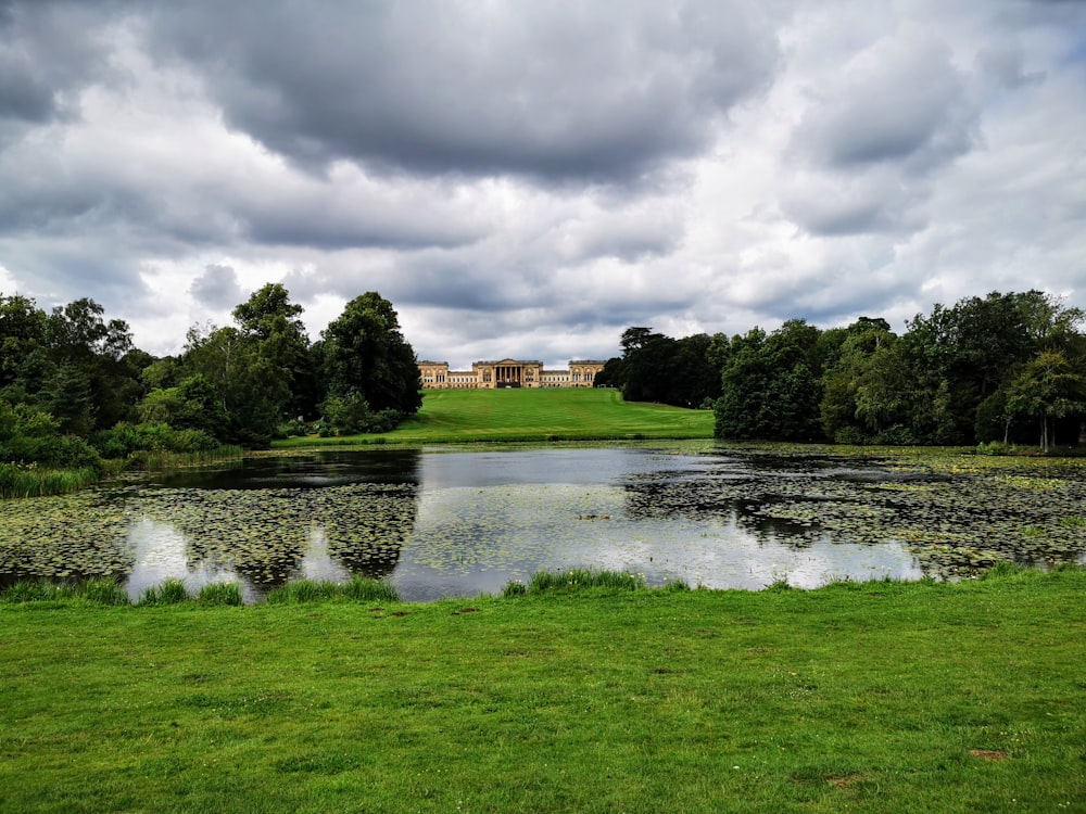 green grass field near river under cloudy sky during daytime