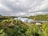 A lush landscape featuring large, geodesic dome structures surrounded by dense greenery and palm trees. Rolling hills covered in forests stretch across the background under an overcast sky.